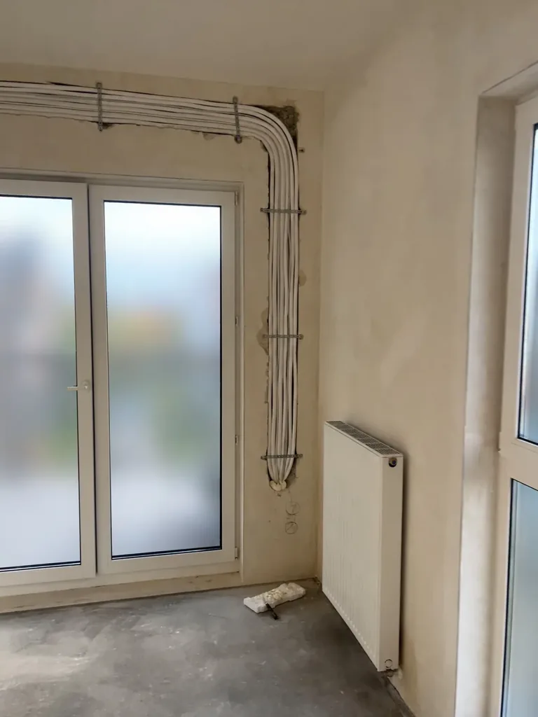 Przebieg instalacji przy ścianie z wyjściem na balkon — kadr z dokumentacji filmowej.
